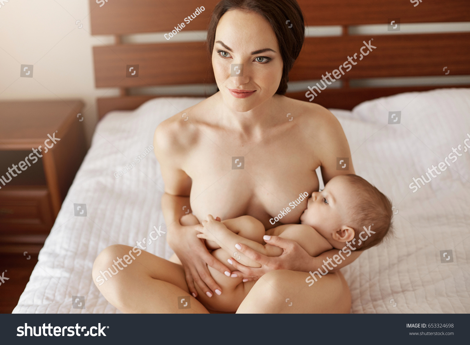 Стоковая фотография 653324698: Young Attractive Nude Mom Breastfeeding Hugg...