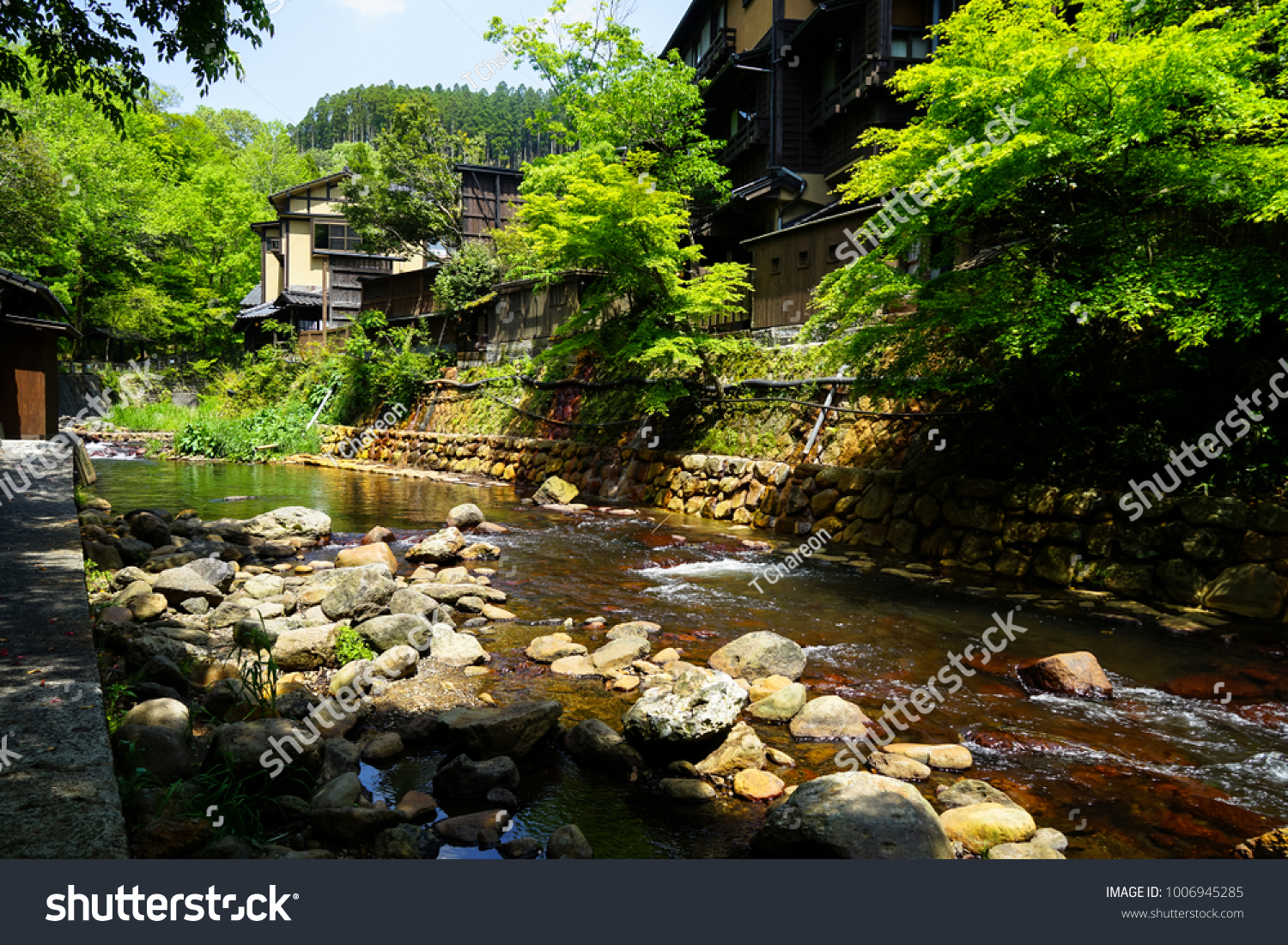 View of fresh river stream, stone bank and natural rock beach with green trees and local buildings in Kurokawa onsen town, Japan #1006945285