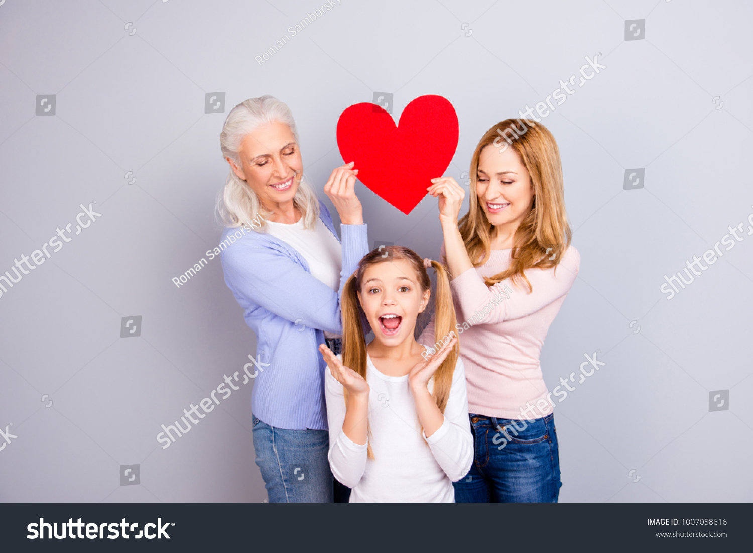 Emotional feeling tenderness gentle warmth concept, Beautiful mum and delightful granny are holding big bright red heart over joy joyful cheerful small girl's head isolated on gray background #1007058616
