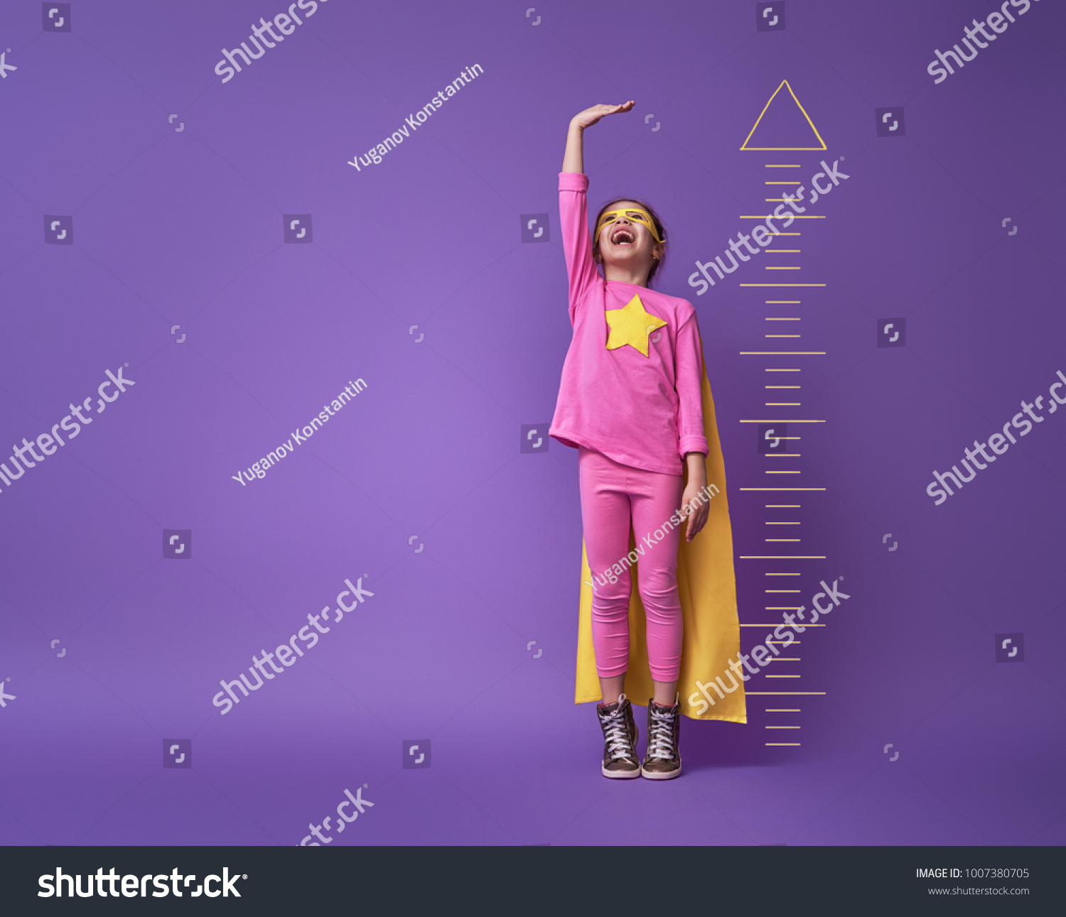 Little child is playing superhero. Kid is measuring the growth on the background of bright ultraviolet wall. Girl power concept. Yellow, pink and  purple colors. #1007380705