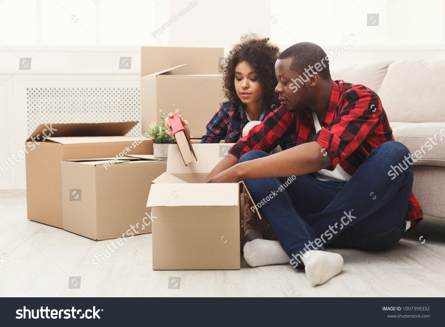 Happy african-american couple unpacking moving boxes and taking out books in new apartment, copy space #1007399332