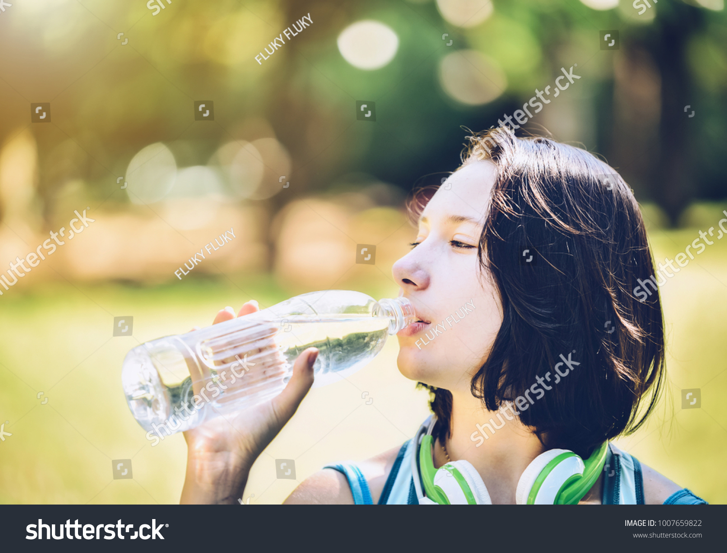 A girl drinking water with thirst after exercise, with a park in the background. #1007659822