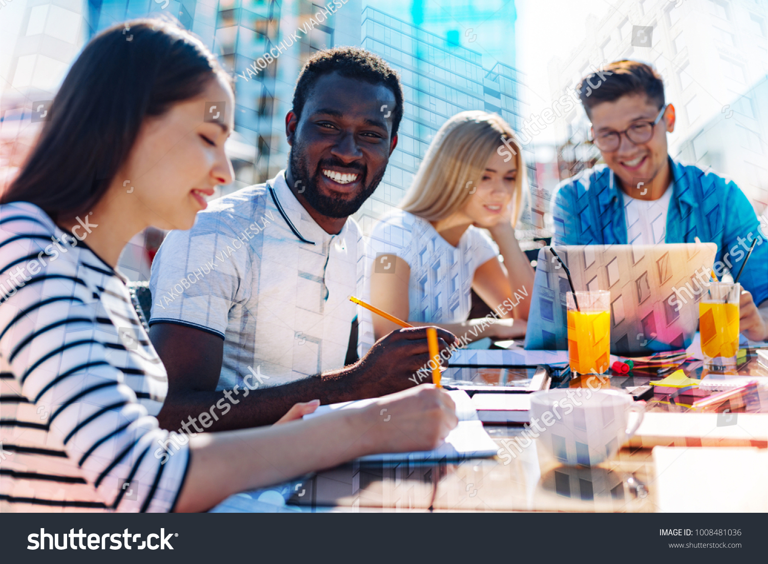 Working together. Handsome cheerful afro-american man smiling and holding a pencil while working with his colleagues on a project #1008481036