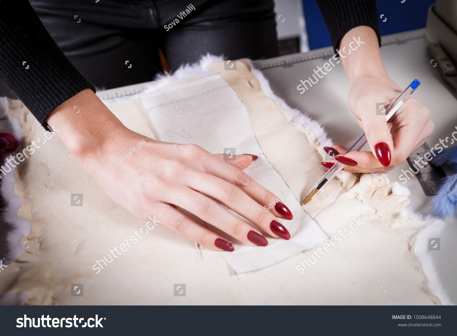 Close-up of a young furrier woman, a seamstress cuts out a piece of white natural fur #1008648844