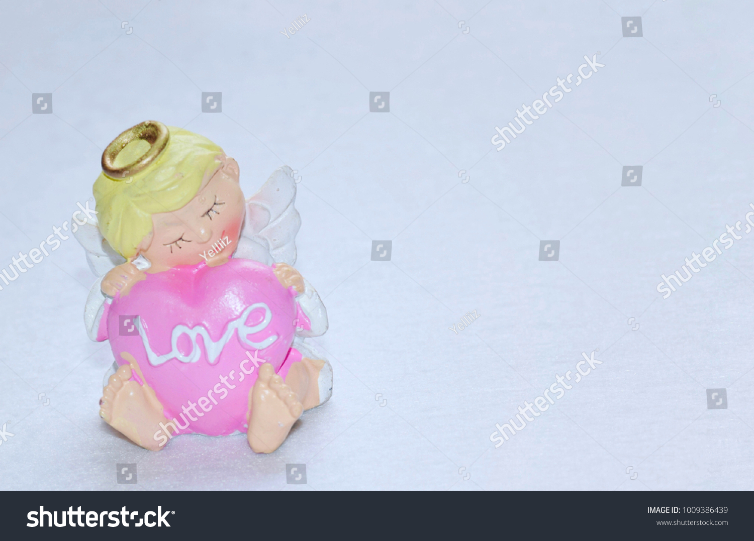 Resin angel doll hugging pink heart shape with Love text on white background, Love concept. #1009386439