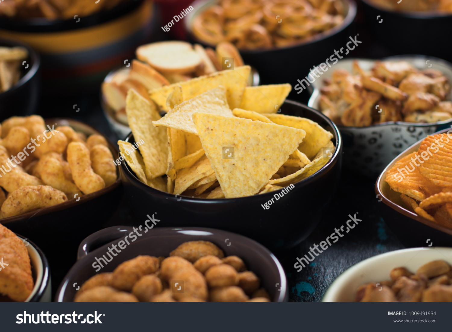 Salty snack including peanuts, potato chips and pretzels served as party food in bowls #1009491934