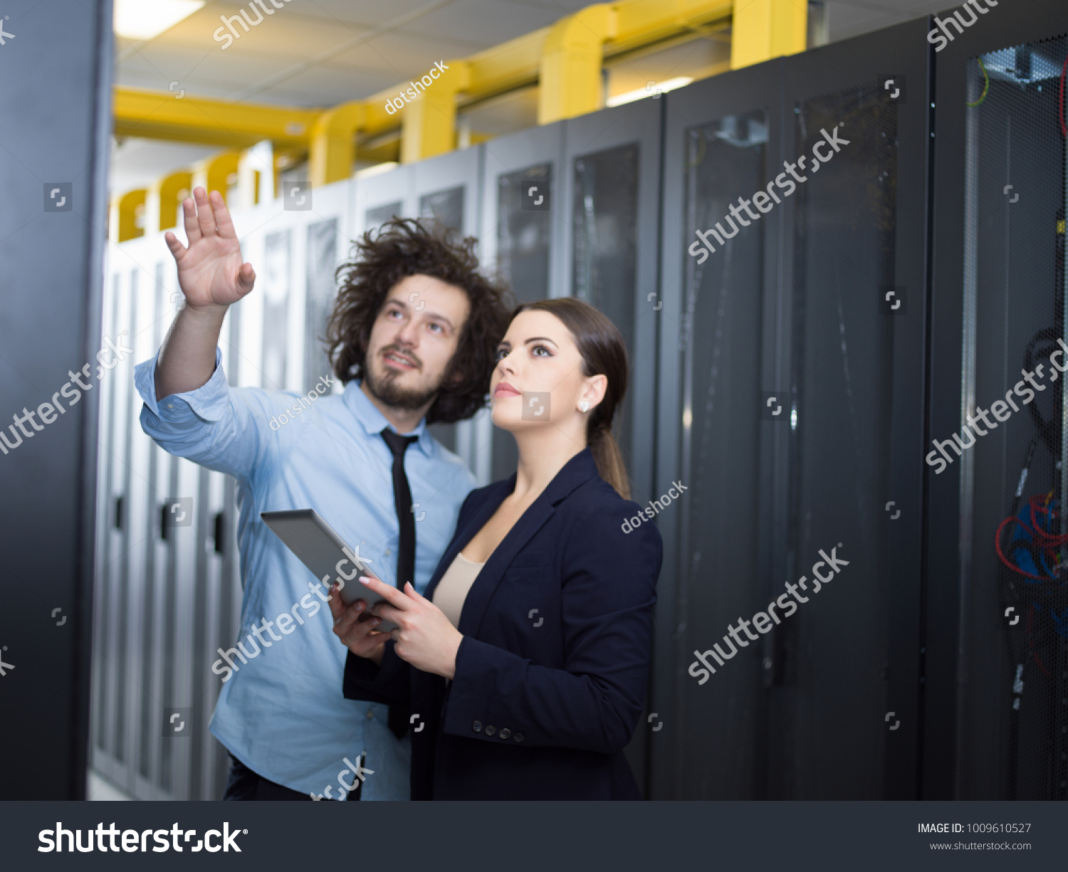 Young IT engineer showing working data center server room to female chief engineer who holding tablet computer #1009610527