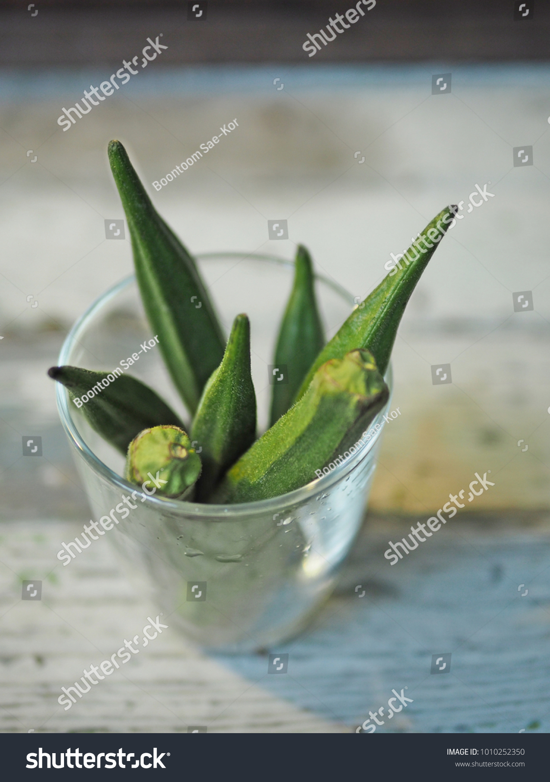 Glass of fresh green okra or lady's fingers or ochro in a glass on vintage wooden background. (close up, selective focus, space for text) #1010252350