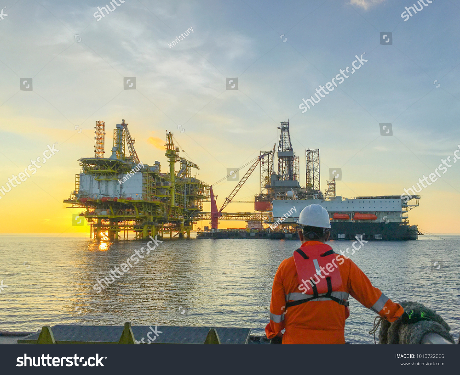 Oil and gas industry. Marine crew standing on supply vessel looking oil and gas platform during sunrise. #1010722066
