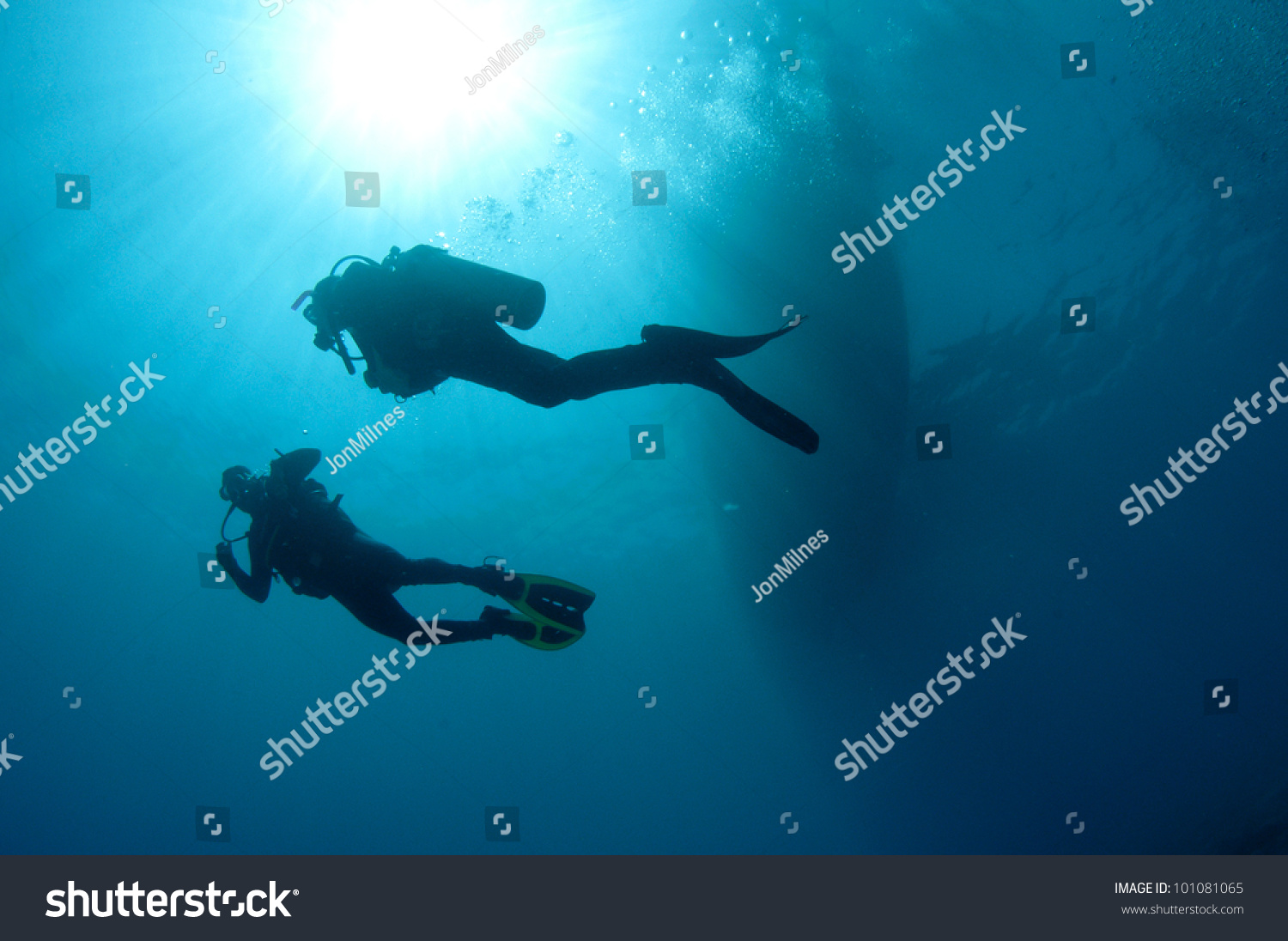 shilouetted scuba divers swim in the deep blue ocean #101081065