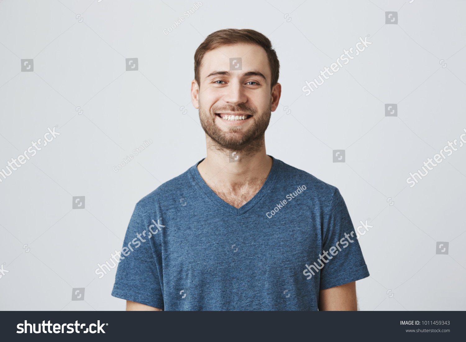 Studio shot of joyfully smiling bearded european male model in blue t-shirt, looking at camera with broad smile. Positive emotions, feelings and reaction #1011459343