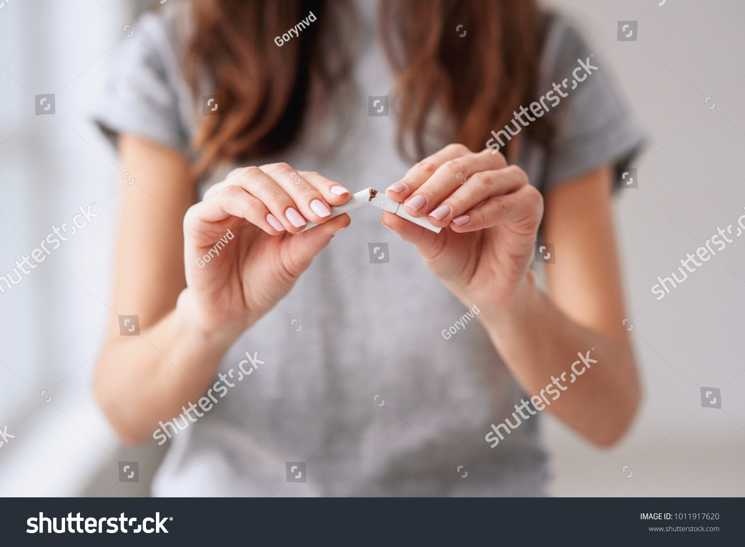 Stop smoking cigarettes concept. Portrait of beautiful smiling girl holding broken cigarette in hands. Happy female quitting smoking cigarettes. Quit bad habit, health care concept. No smoking. #1011917620