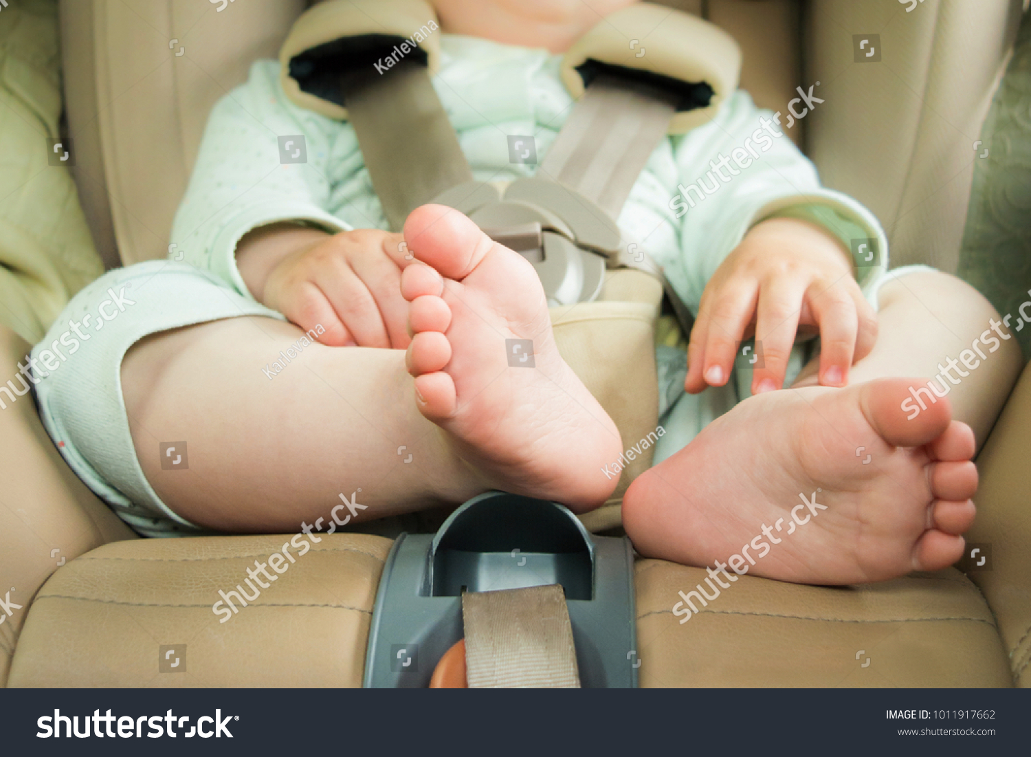 Small baby sitting in special car seat with safety seabelts, Safety in car concept, protection of child in travel, children feet in baby seat #1011917662