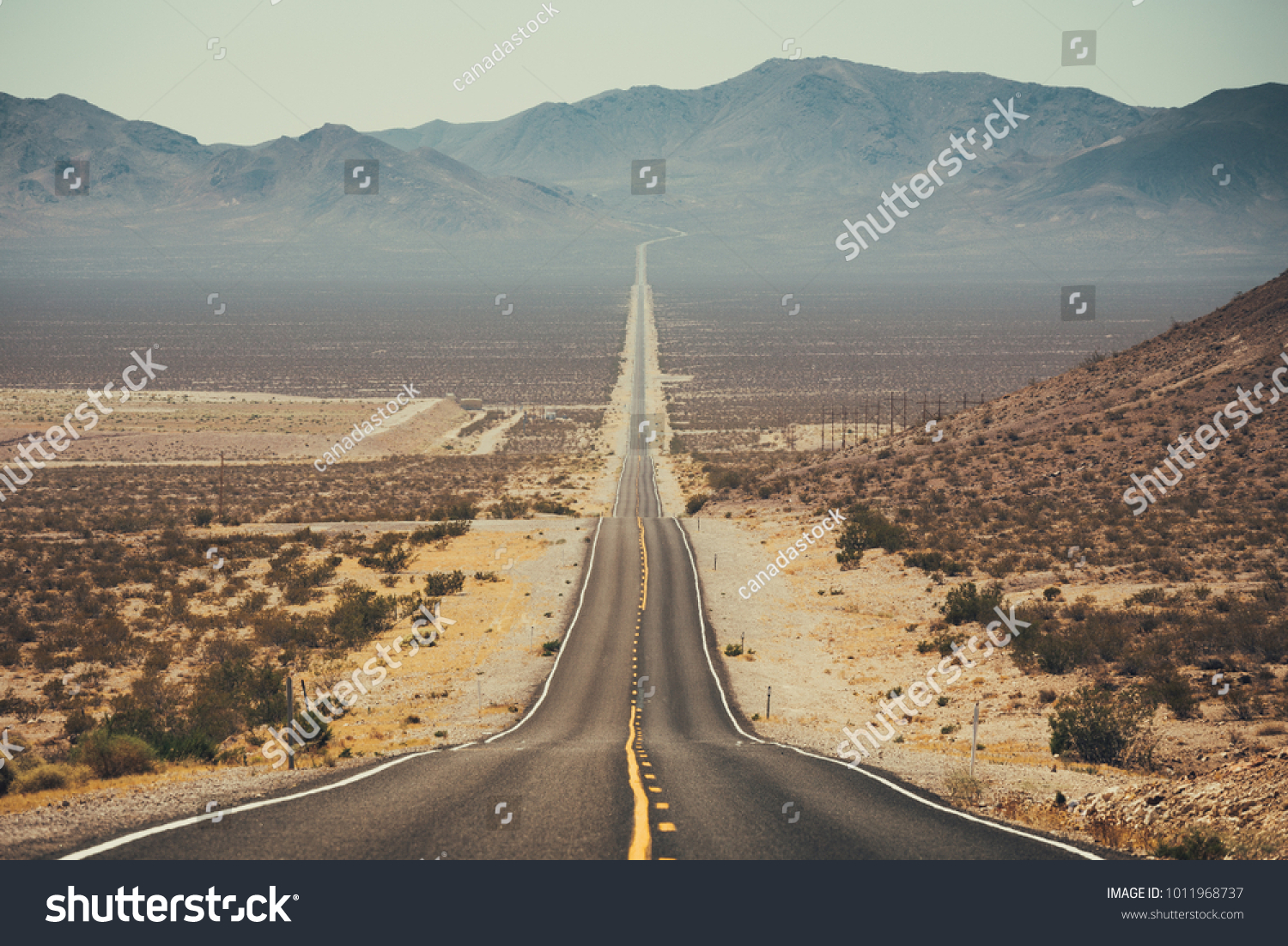 Classic panorama view of an endless straight road running through the barren scenery of the American Southwest with extreme heat haze on a beautiful sunny day with blue sky in summer #1011968737