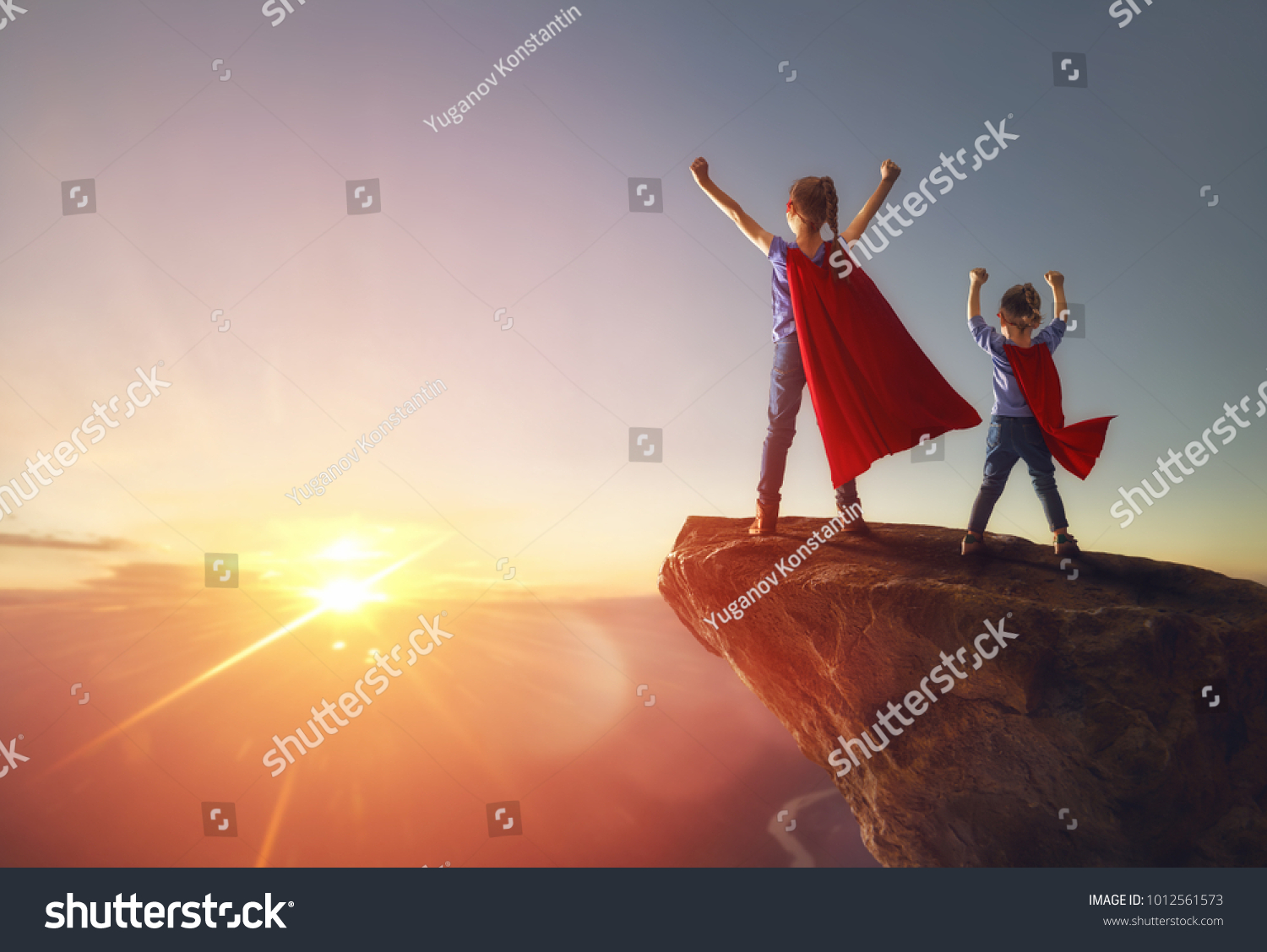 Two little children are playing superhero. Kids on the background of sunset sky. Girl power concept #1012561573