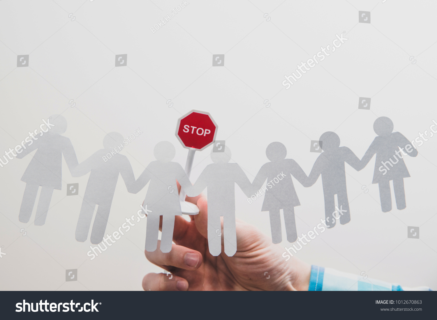 Hand holding a stop sign over one of the people in the crowd. Characters cut from paper. The boss or superior orders to stop the bad practices. Warns the employee against bad work. #1012670863