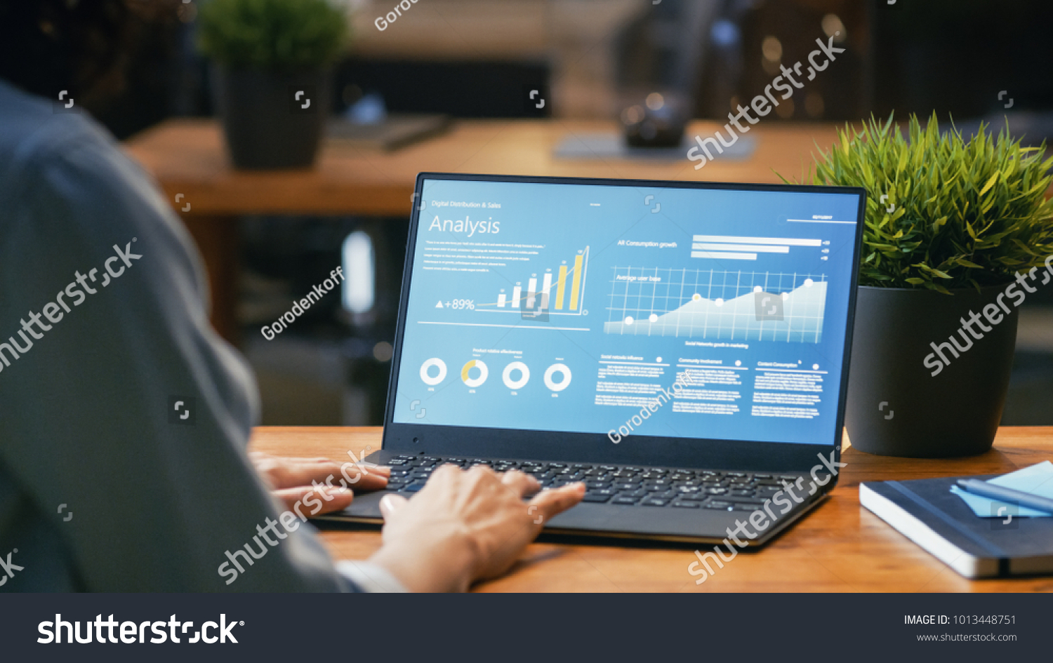 Female Analyst at Her Desk Works on a Laptop Showing Statistics, Graphs and Charts. She Works on the Wooden Table in Creative Office. Over the Shoulder Footage. #1013448751