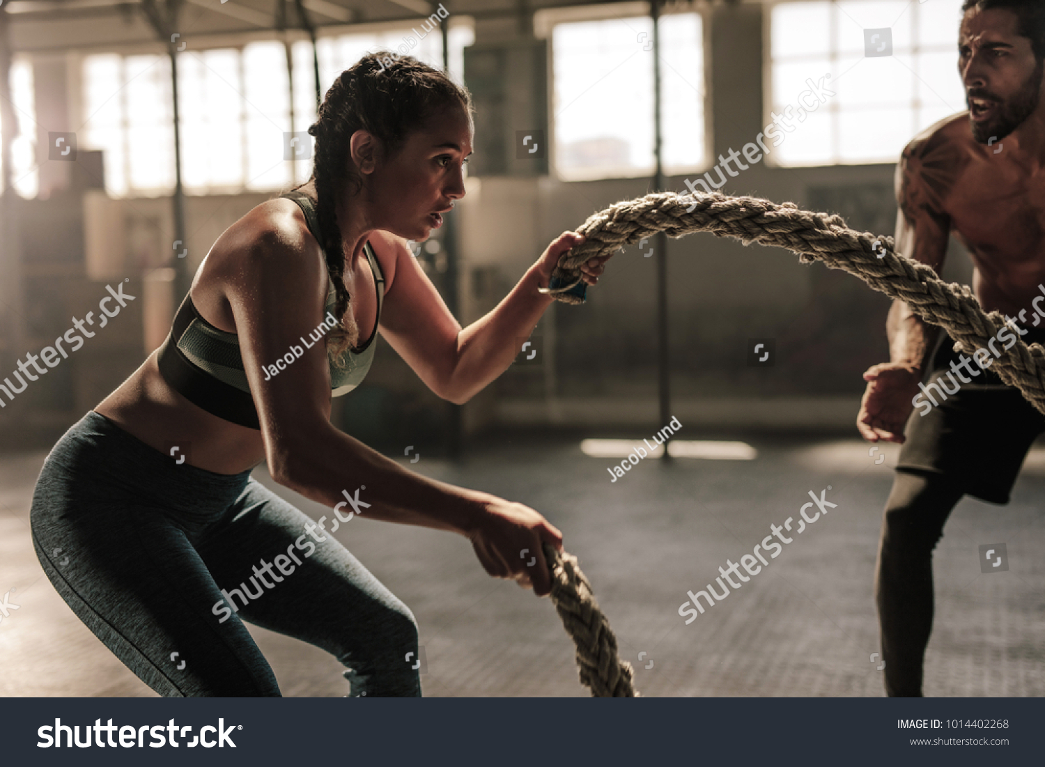Strong woman exercising with battle ropes at the gym with male trainer. Athlete doing battle rope workout at gym with instructor. #1014402268