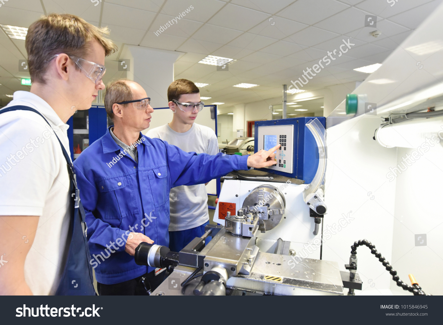 young apprentices in technical vocational training are taught by older trainers on a cnc lathes machine #1015846945