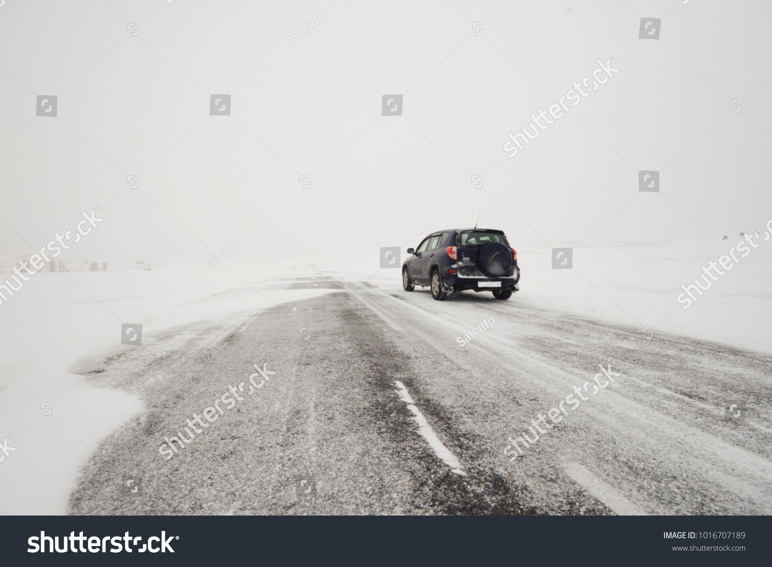 snow-covered fields and a road in winter during a blizzard and a car #1016707189