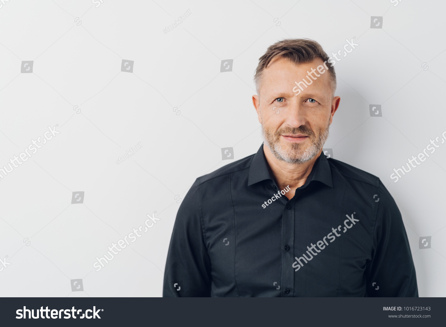 Head and shoulders portrait of a bearded middle-aged man looking thoughtfully at the camera over a white studio background with copy space