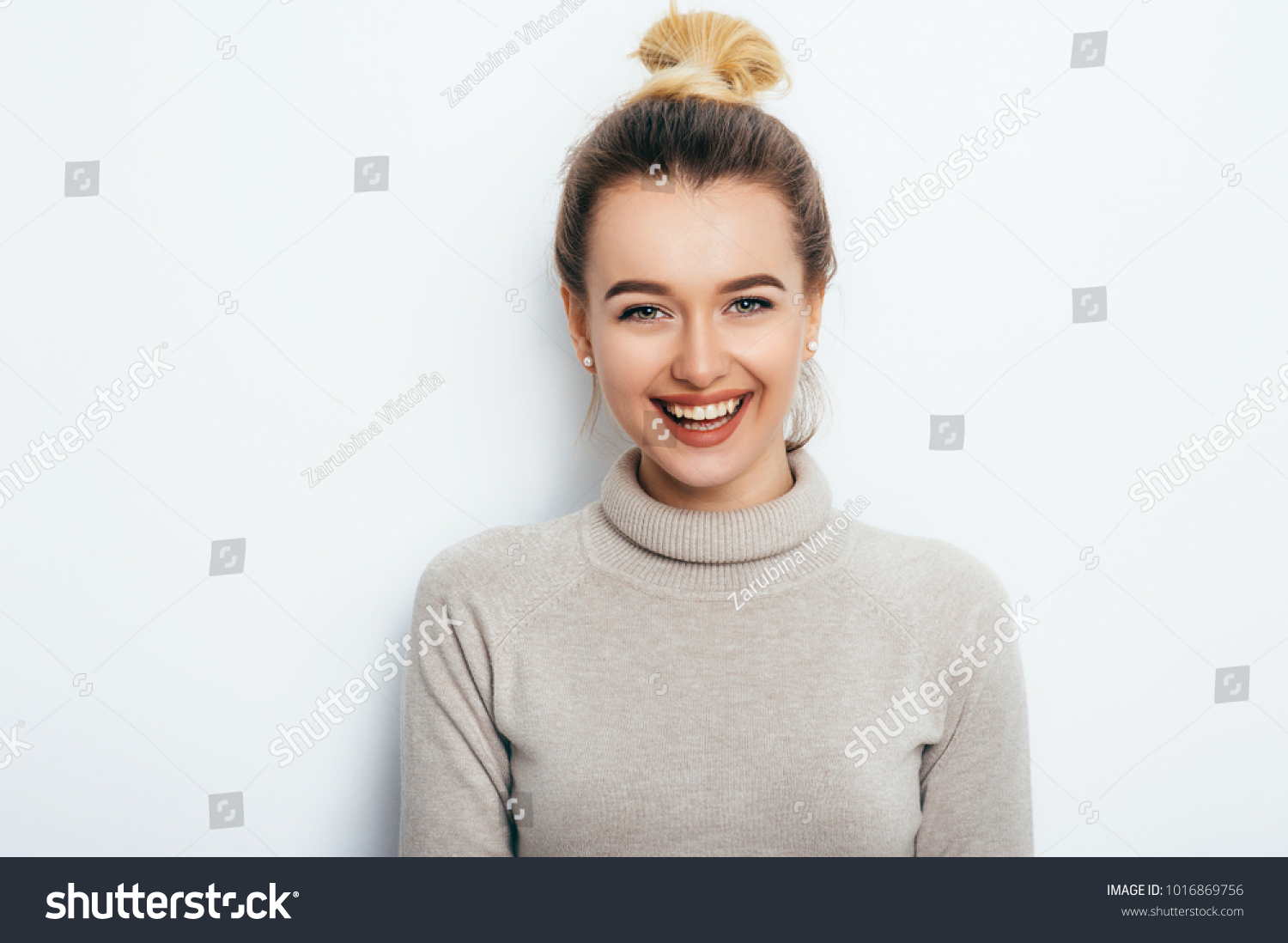 Horizontal portrait of cheerful woman with appealing smile, having hair bun wearing in sweater isolated over white background.  Beautiful female showing her pleasant emotions. People Beauty Fashion  #1016869756