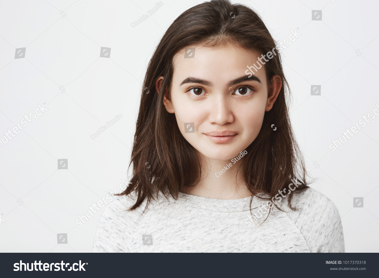 Portrait of cute naive european lop-eared girl with cute smile and mysterious look, over white background. Beautiful brunette makes photo for her profile in social network #1017370318