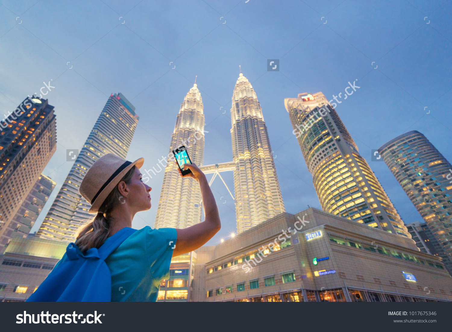 Travel and technology. Young  woman taking photo with her smartphone of Petronas Twins Towers in Kuala-Lumpur at evening, Malaysia, 23 November 2015. #1017675346