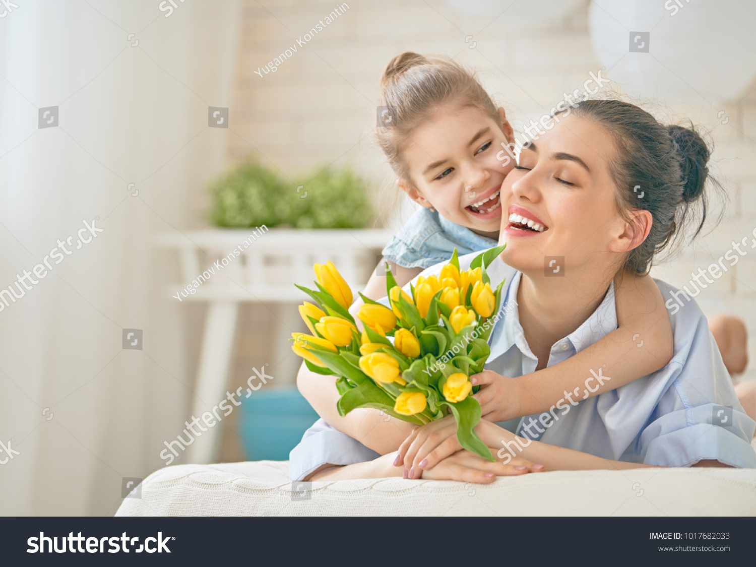 Happy mother's day! Child daughter is congratulating mom and giving her flowers tulips. Mum and girl smiling and hugging. Family holiday and togetherness. #1017682033