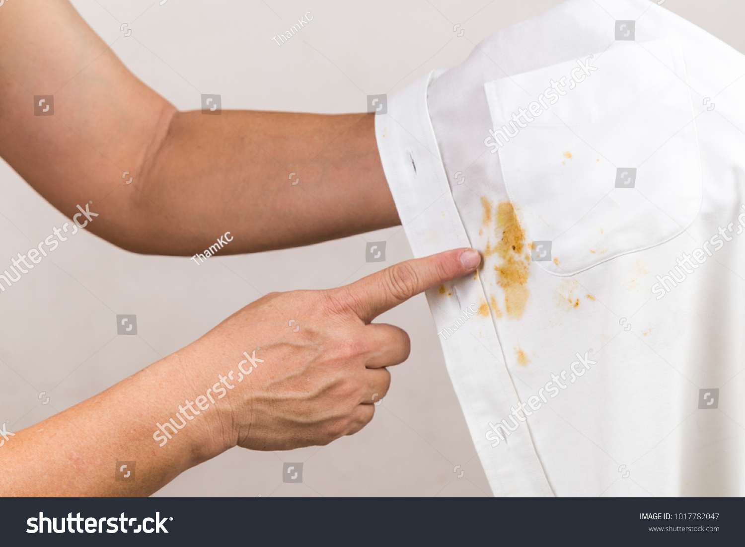 Frustrated person pointing to spilled curry stain on white shirt #1017782047