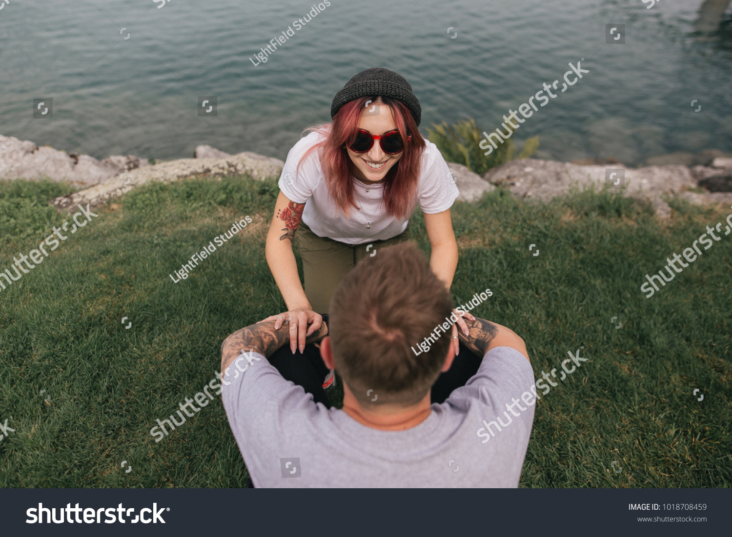 high angle view of happy young couple looking at each other while sitting on green grass near lake #1018708459