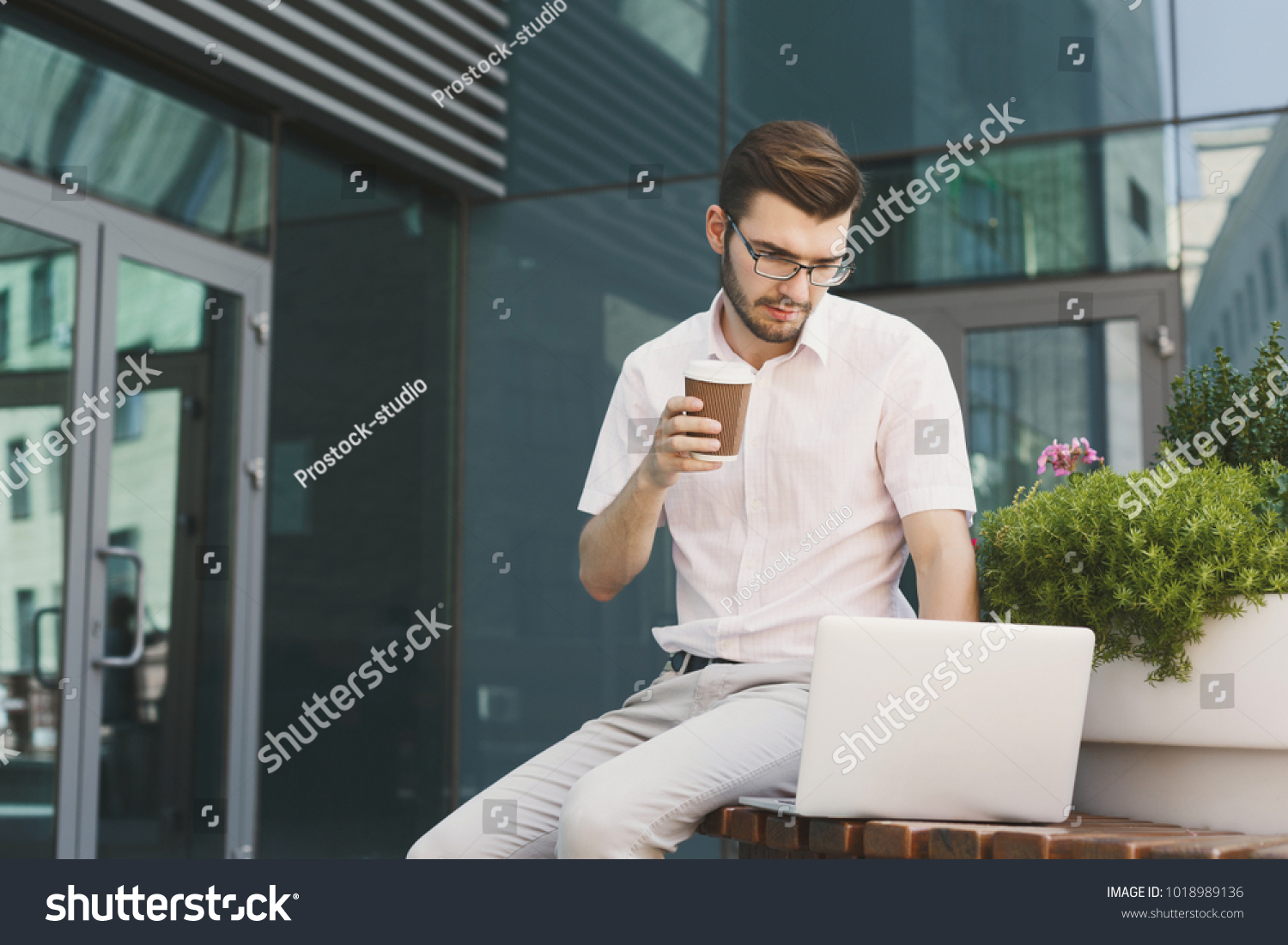 Serious businessman working on laptop. Young concentrated insurance agent checking email on computer, sitting on stairs outdoors in urban area, copy space #1018989136
