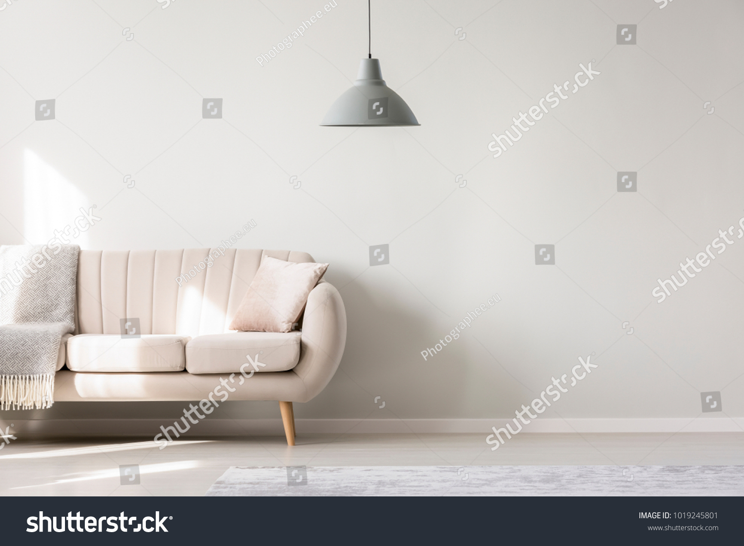 Beige sofa against white, empty wall with copy space in simple living room interior with lamp #1019245801