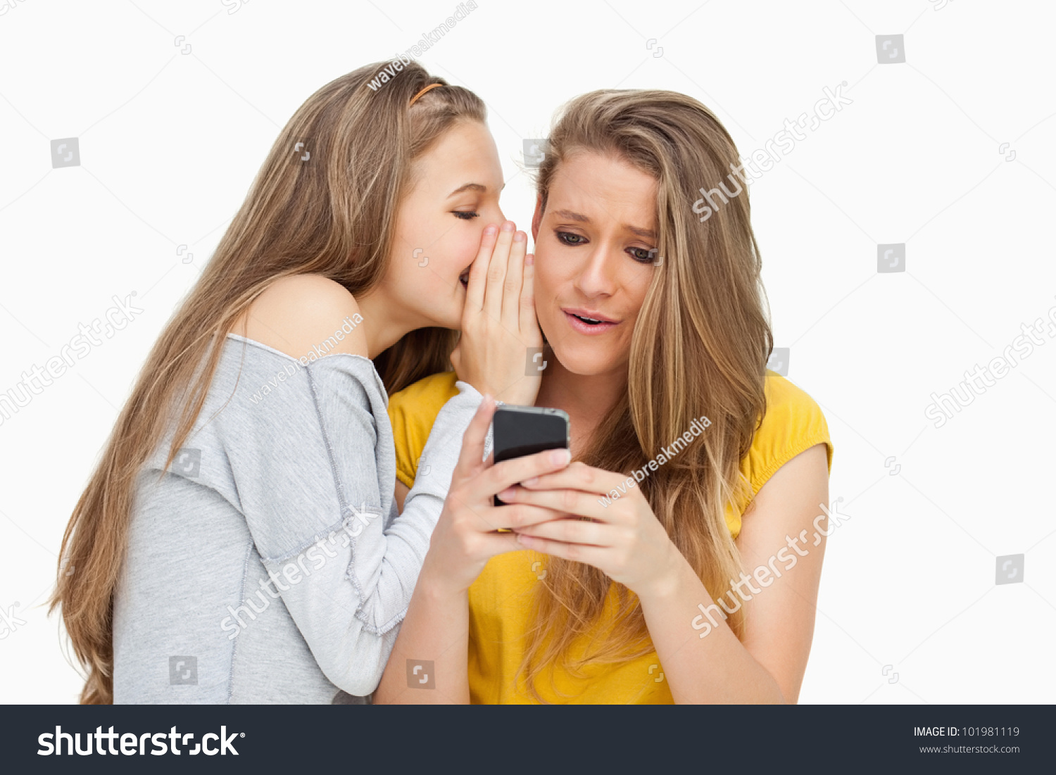 Student whispering to her friend who's texting on her phone against white background #101981119