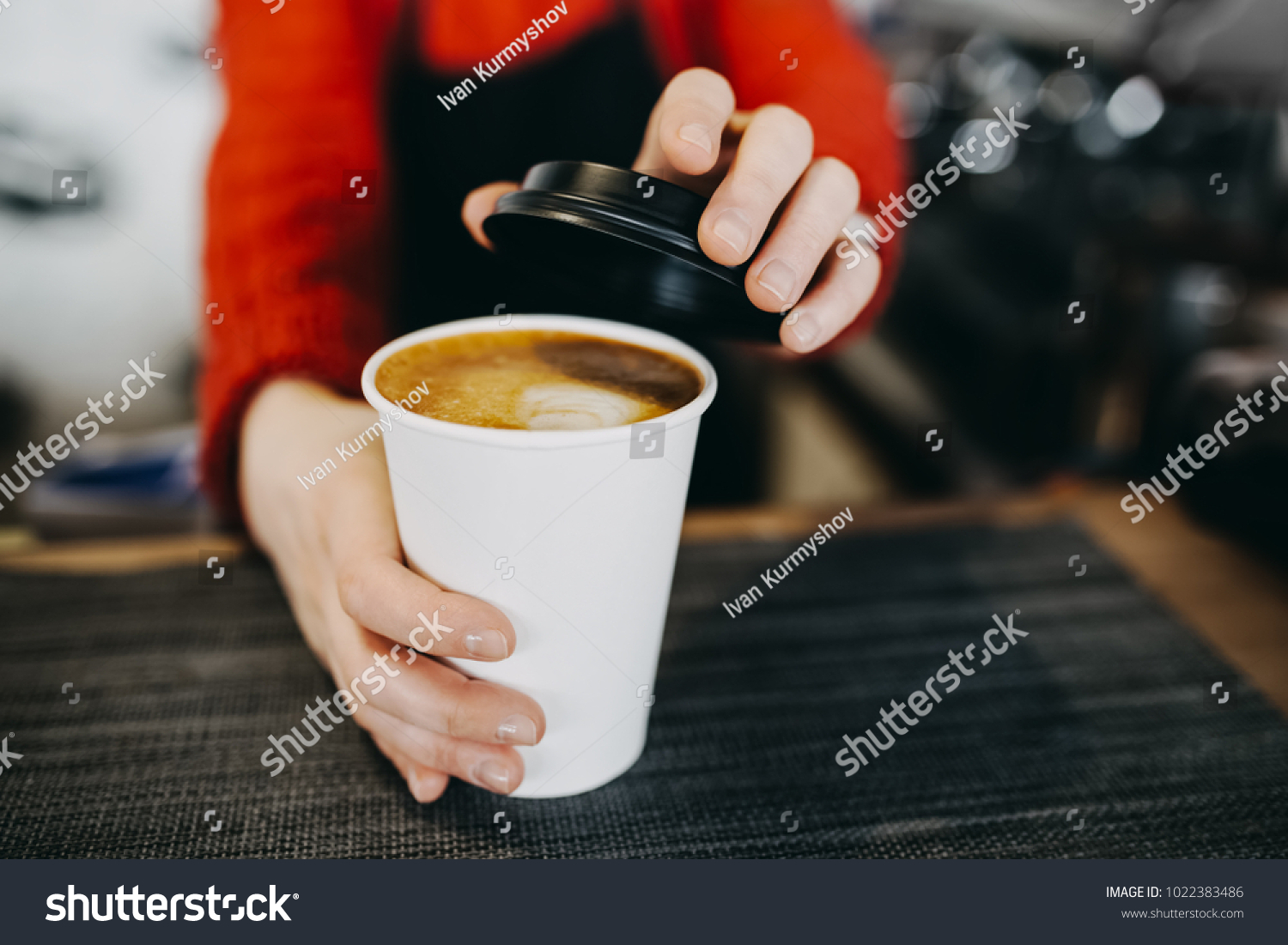 Barista in apron is holding in hands hot cappuccino in white takeaway paper cup. Coffee take away at cafe shop #1022383486