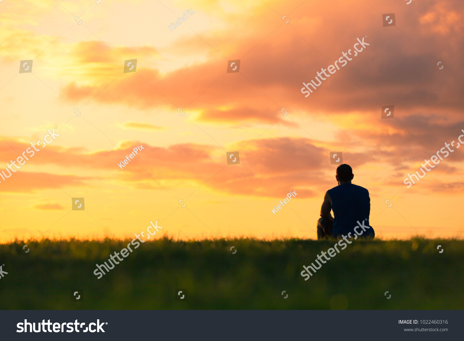 Man sitting watching sunset. Enjoying a peaceful moment, thinking, getting away from it all concept.  #1022460316