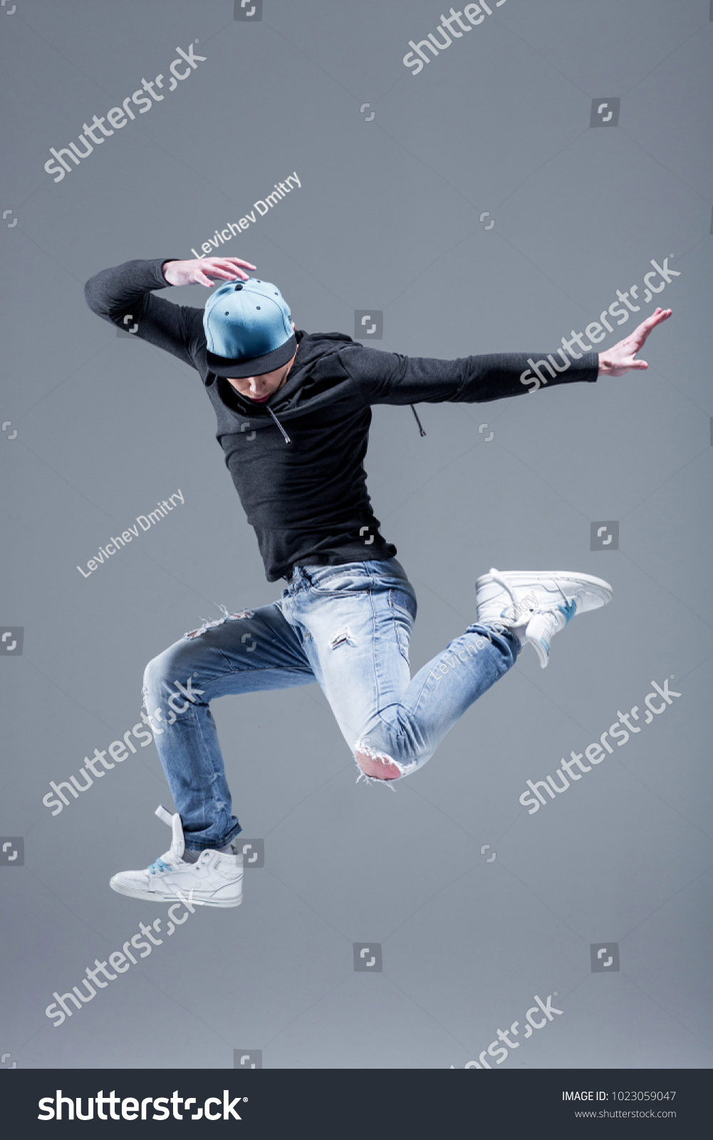 Active young beautiful hip-hop dancer man jump in fly at studio, copy space, motion shot. Grey background #1023059047
