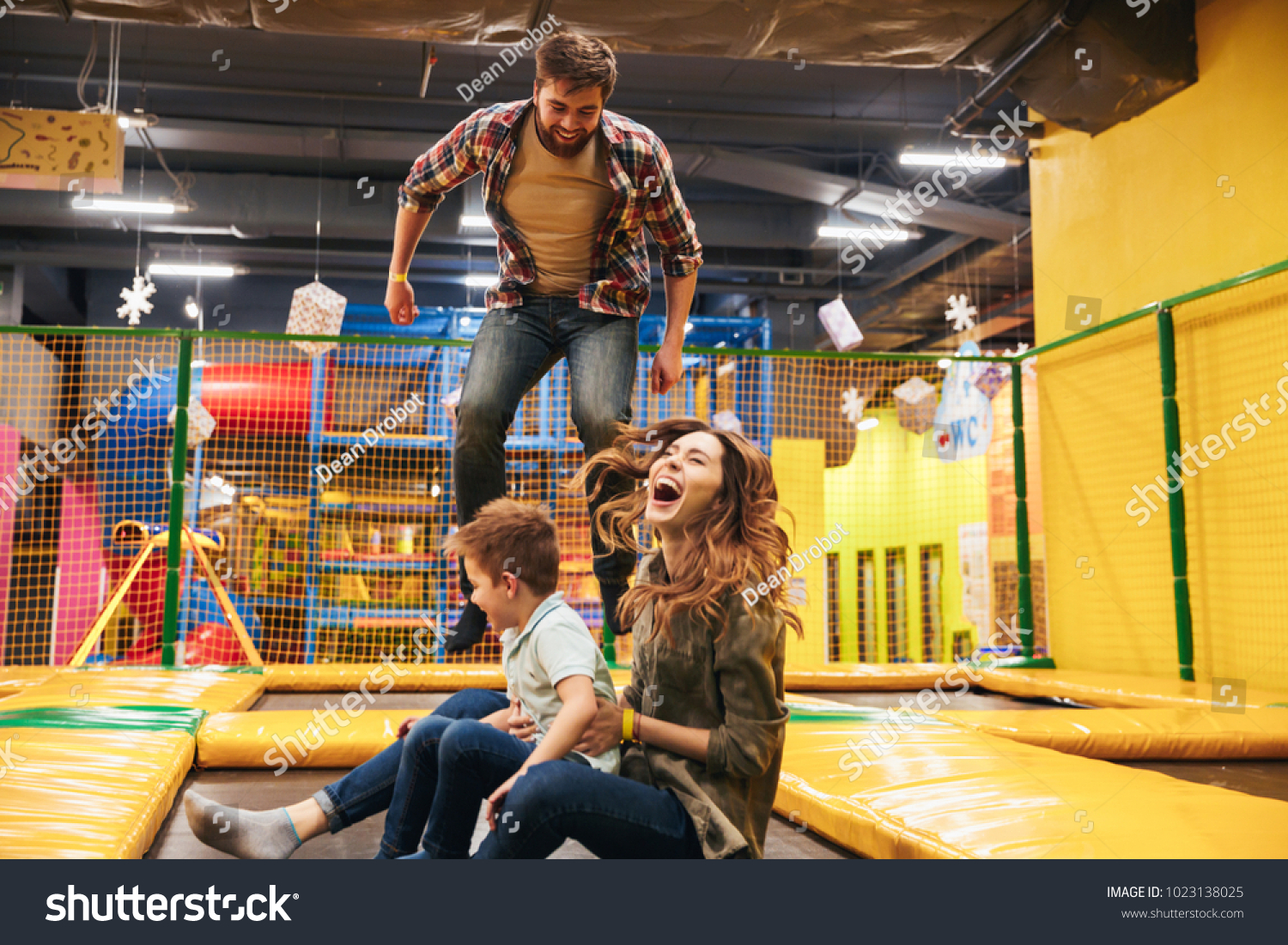 Happy young family with their little son jumping on a trampoline together at the entertainment centre #1023138025