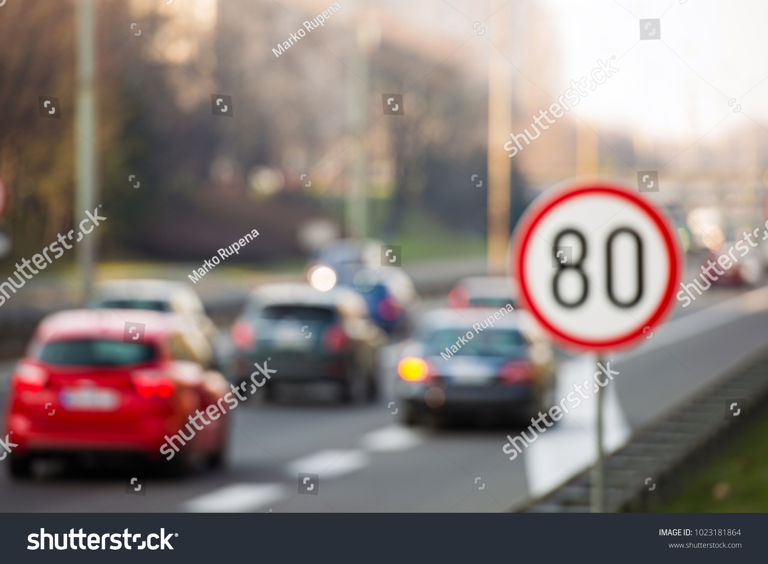 Defocused image of speed limit sign showing 80 km/h speed limit with a traffic in the background #1023181864