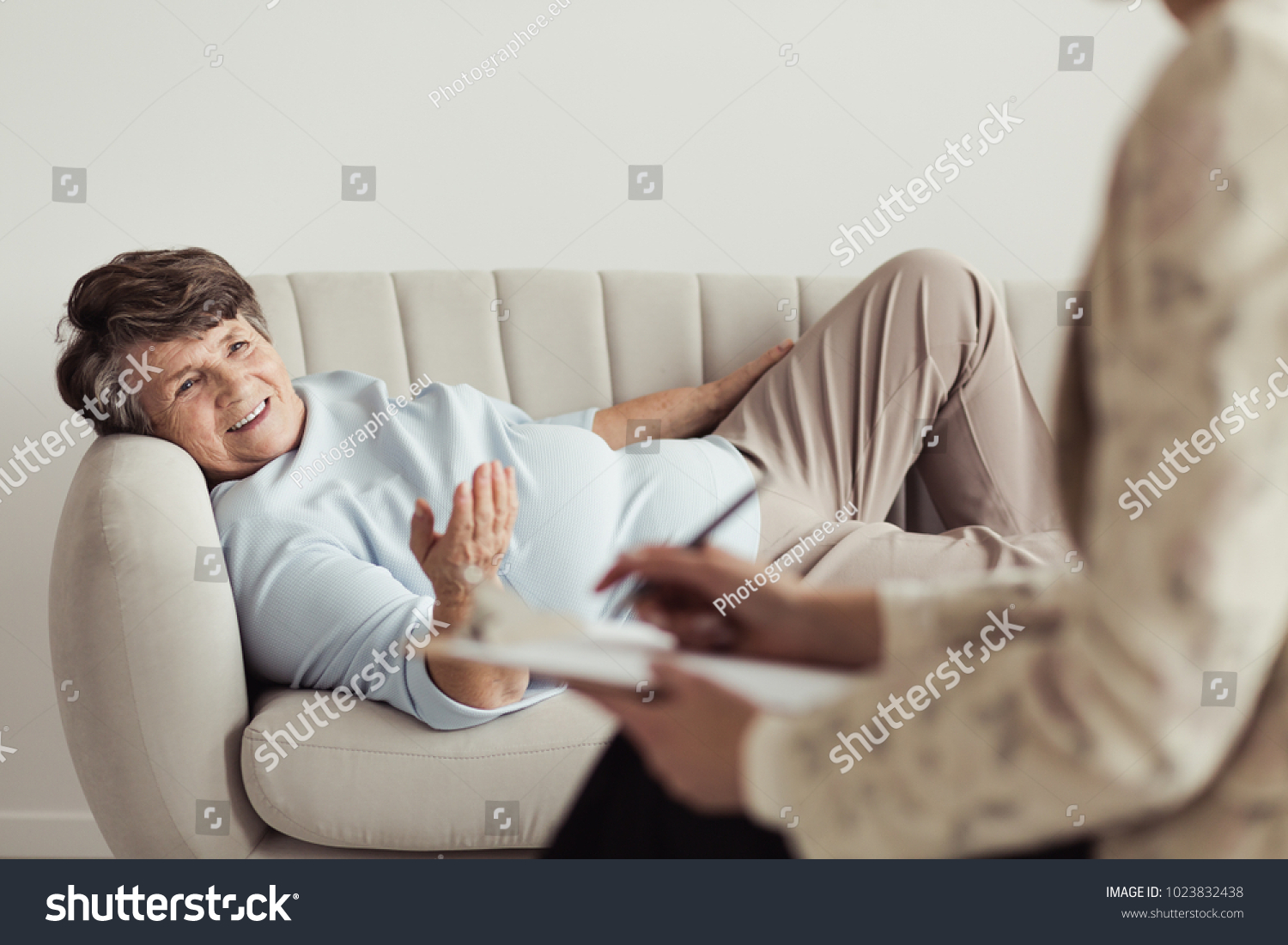 Satisfied elderly woman lying on a settee and talking with a counselor during her appointment #1023832438