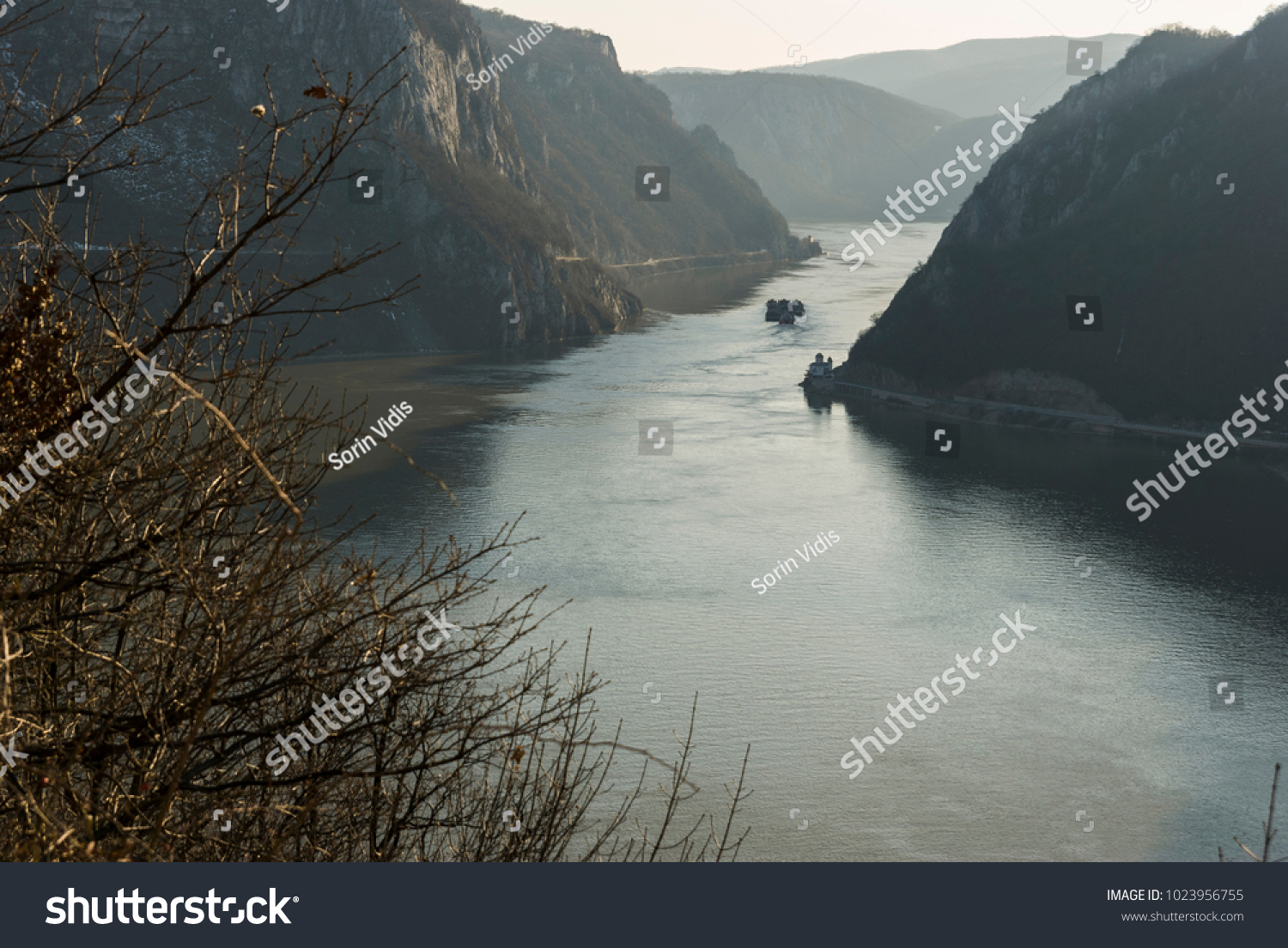 Danube between mountains/Narrow natural channel on the Danube river between the Carpathian mountains that constitutes the border between Romania and Serbia, where a barge is passing by a small church. #1023956755