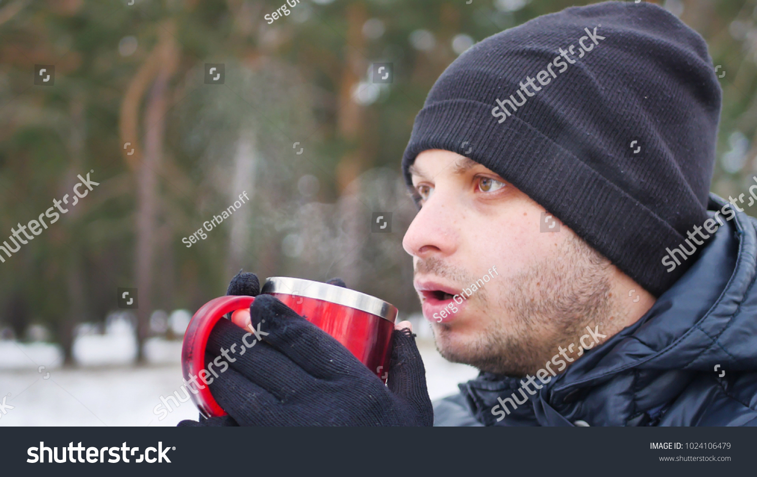 Portrait of cheerful attractive young man drinking hot tea outdoors in winter #1024106479
