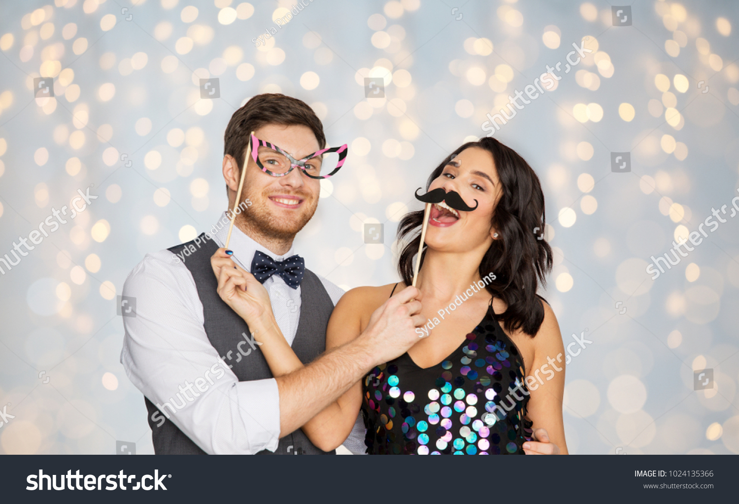 celebration, fun and holidays concept - happy couple posing with party props over festive lights background #1024135366