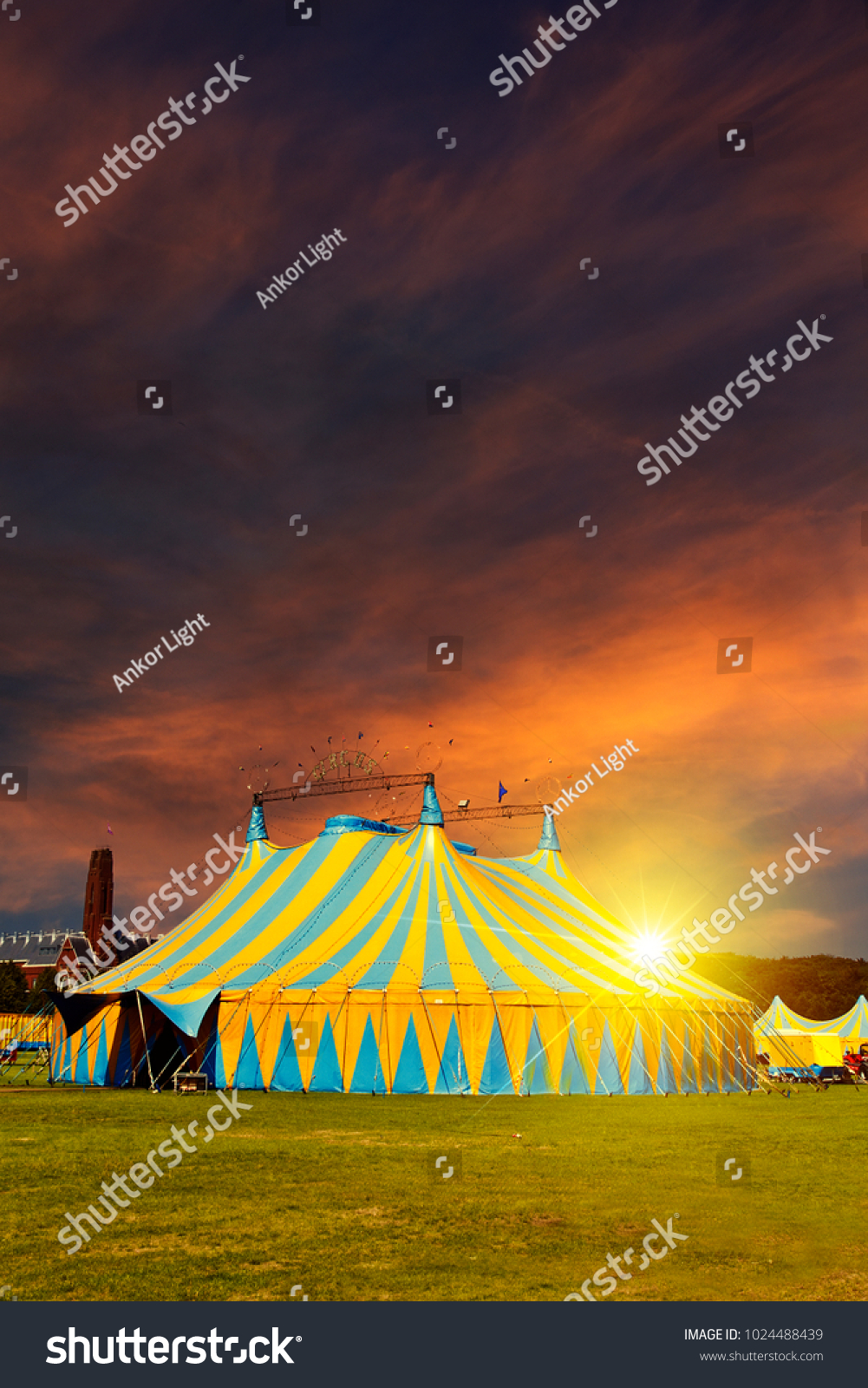 Nonamed circus tent under a warn sunset and chaotic sky without the name of the circus company which is cloned out and replaced by the metallic structure #1024488439