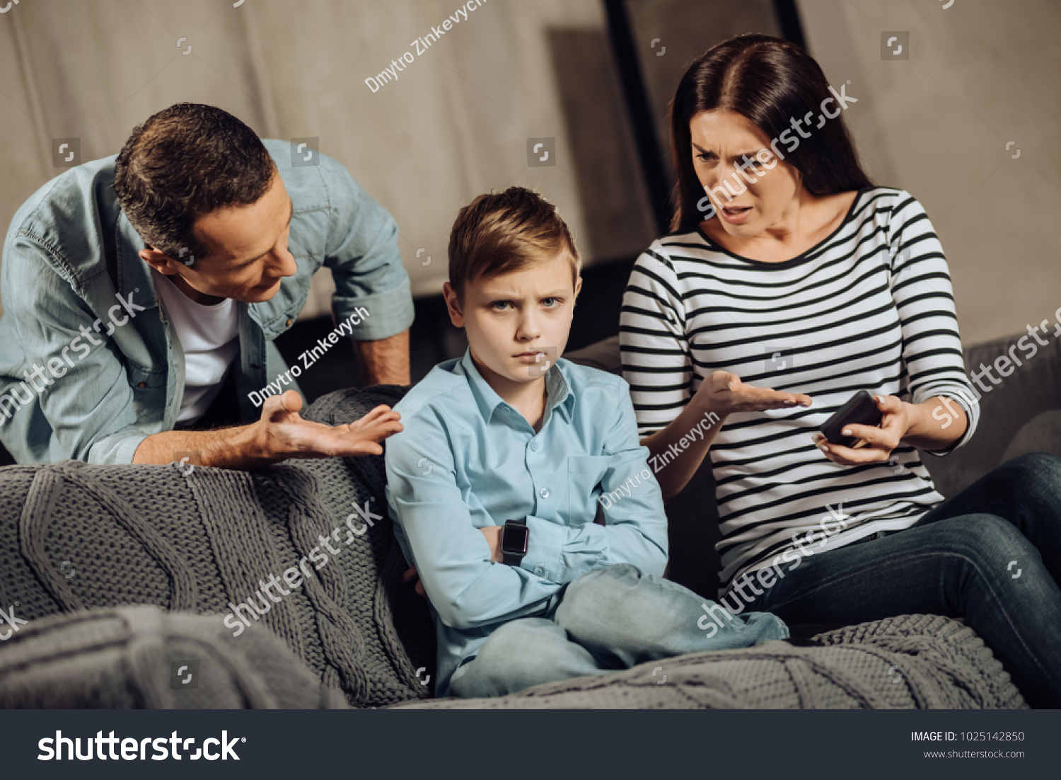 Clear explanation. Strict young parents telling their son about the drawbacks of binge-playing on the phone while the boy, scolding him, while the boy looking offended #1025142850