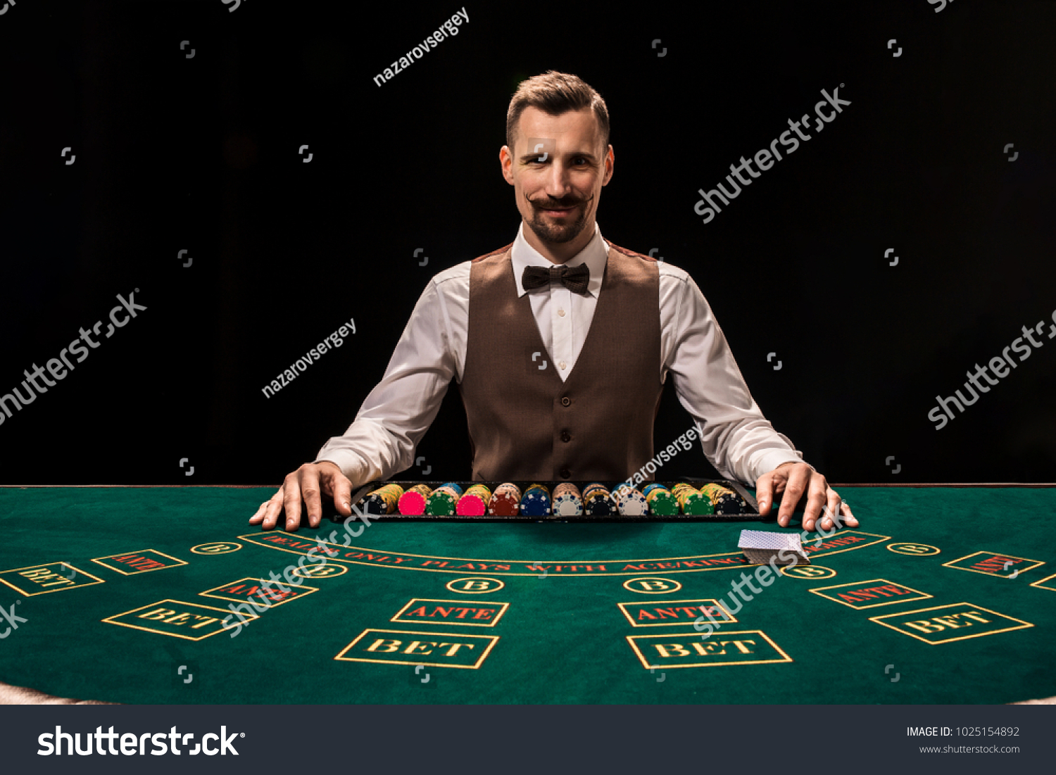 Portrait of a croupier is holding playing cards, gambling chips on table. Black background #1025154892