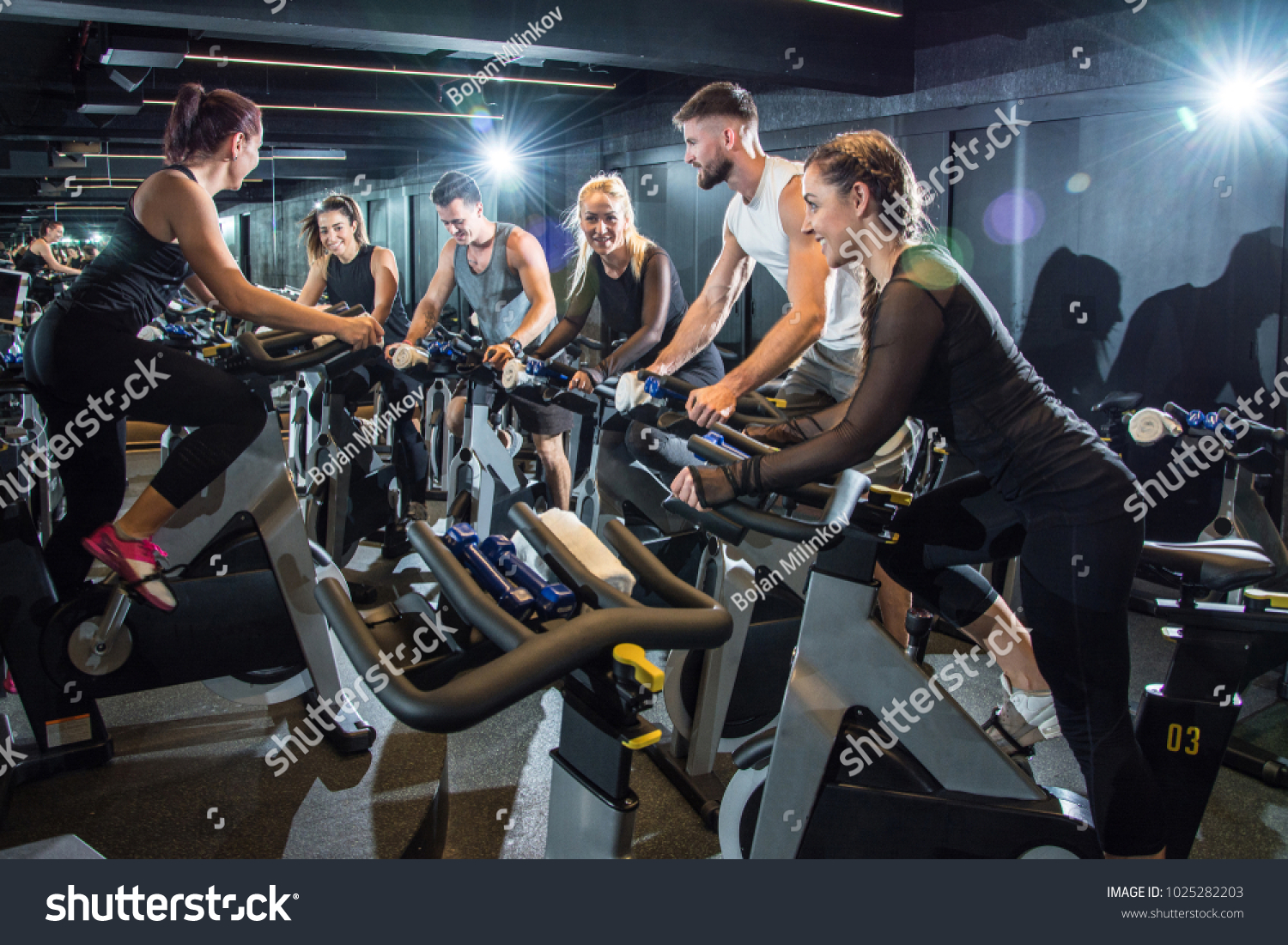 Group of attractive women and men pedaling on a stationary bikes at the gym. #1025282203