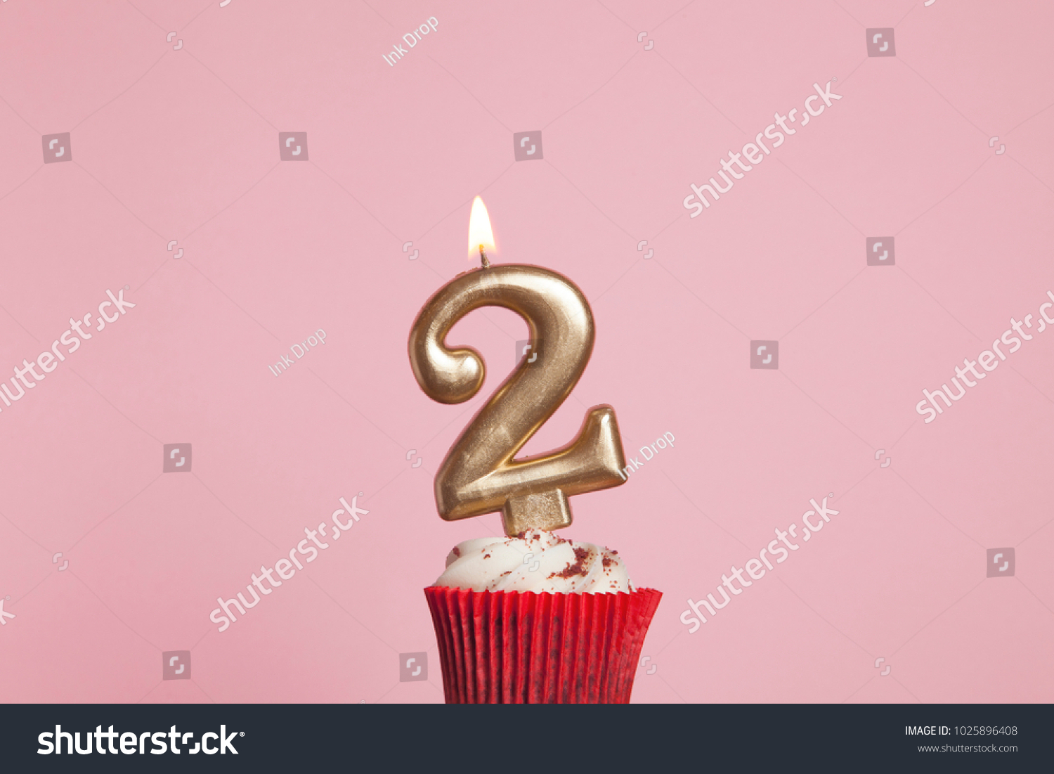 Number 2 gold candle in a cupcake against a pastel pink background