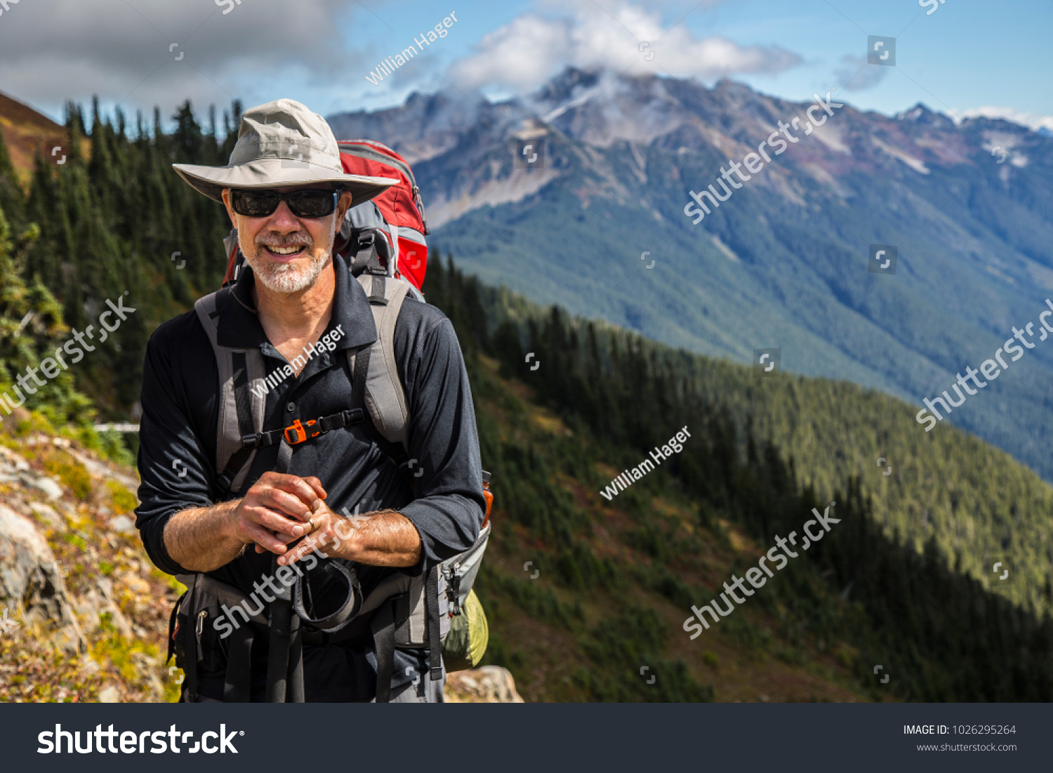 Hiker poses in front of mountain peaks range hiking backpacker old older aarp strong strength vital energetic landscape photography portrait background colorful adventure retired retirement outdoor  #1026295264