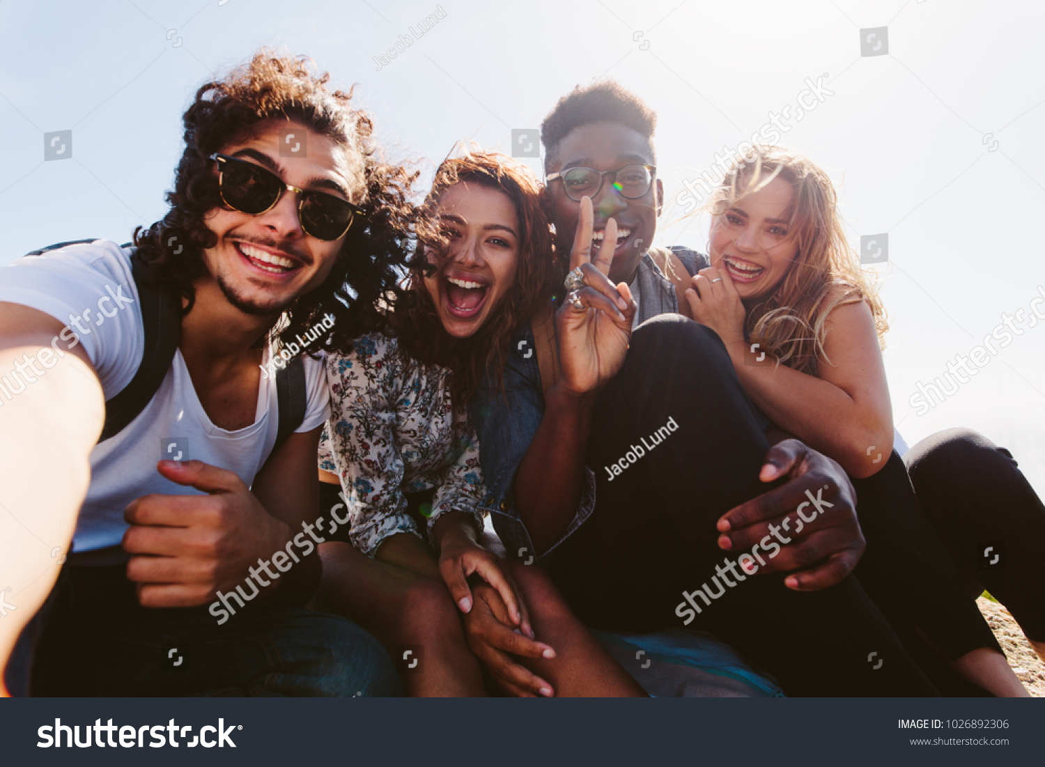 Excited young friends taking selfie outdoors. Diverse group of men and women sitting together and taking self portrait on their holiday. #1026892306